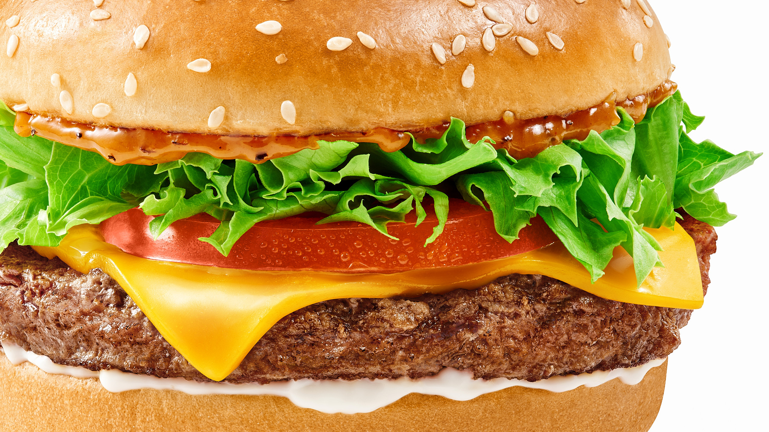 Close-up of a beef burger with lettuce, tomato, melted cheese and spicy sauce on a sesame bun