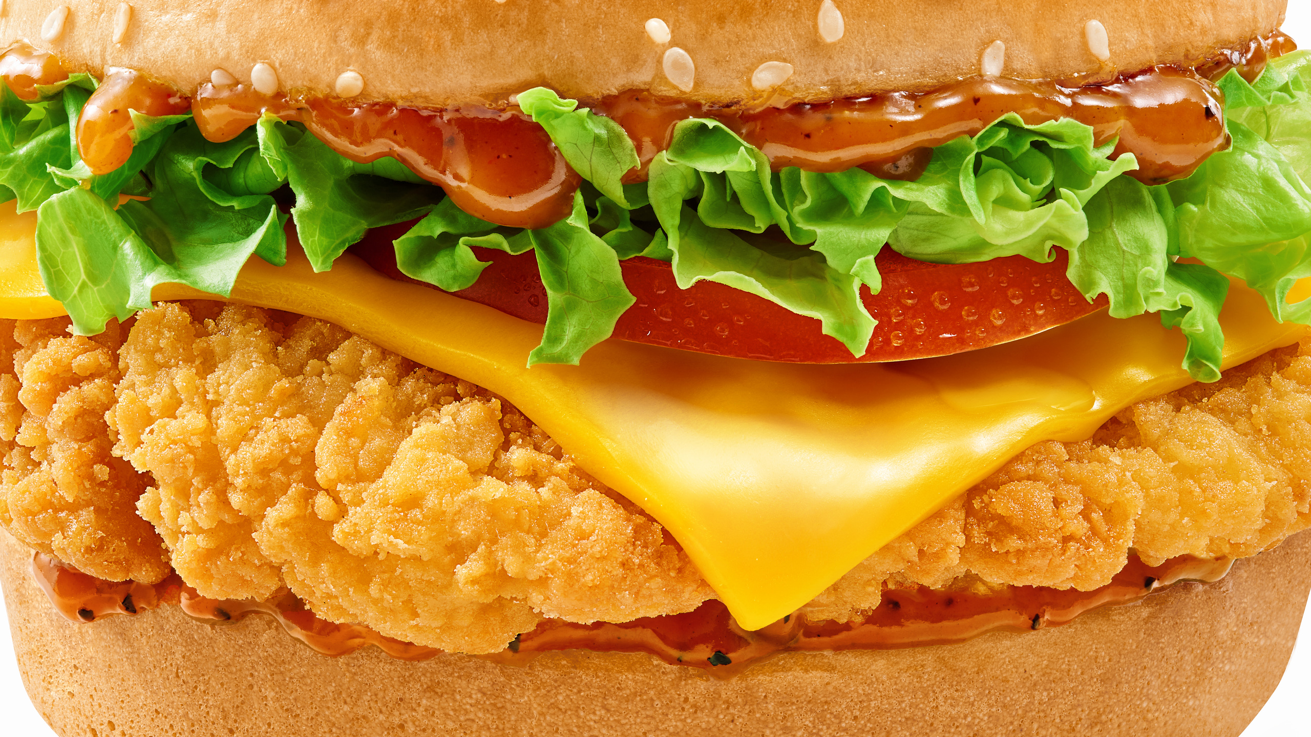 Close-up of crispy chicken burger with melted cheese, lettuce and spicy sauce on a sesame bun
